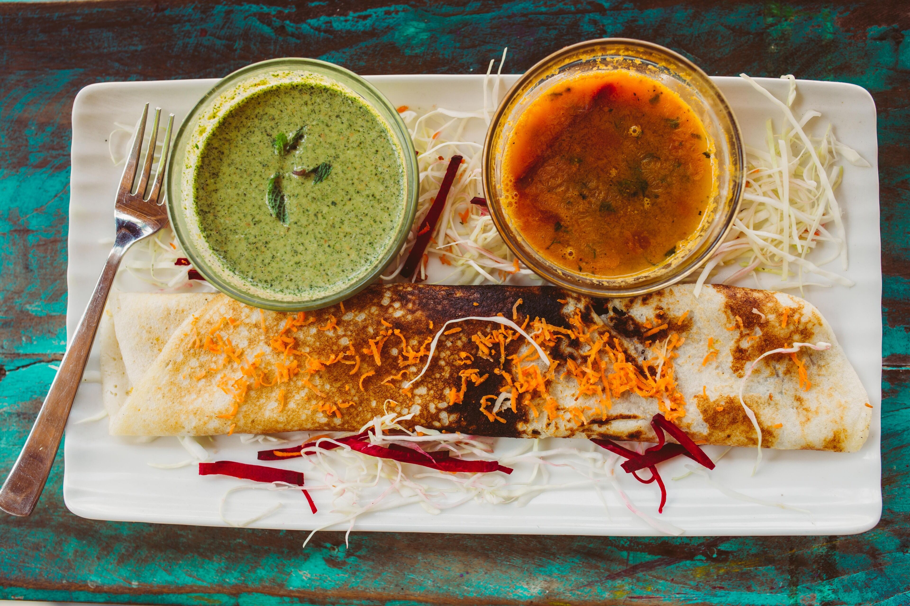 A plate with a rolled dish, two bowls of sauce, and shredded vegetables.