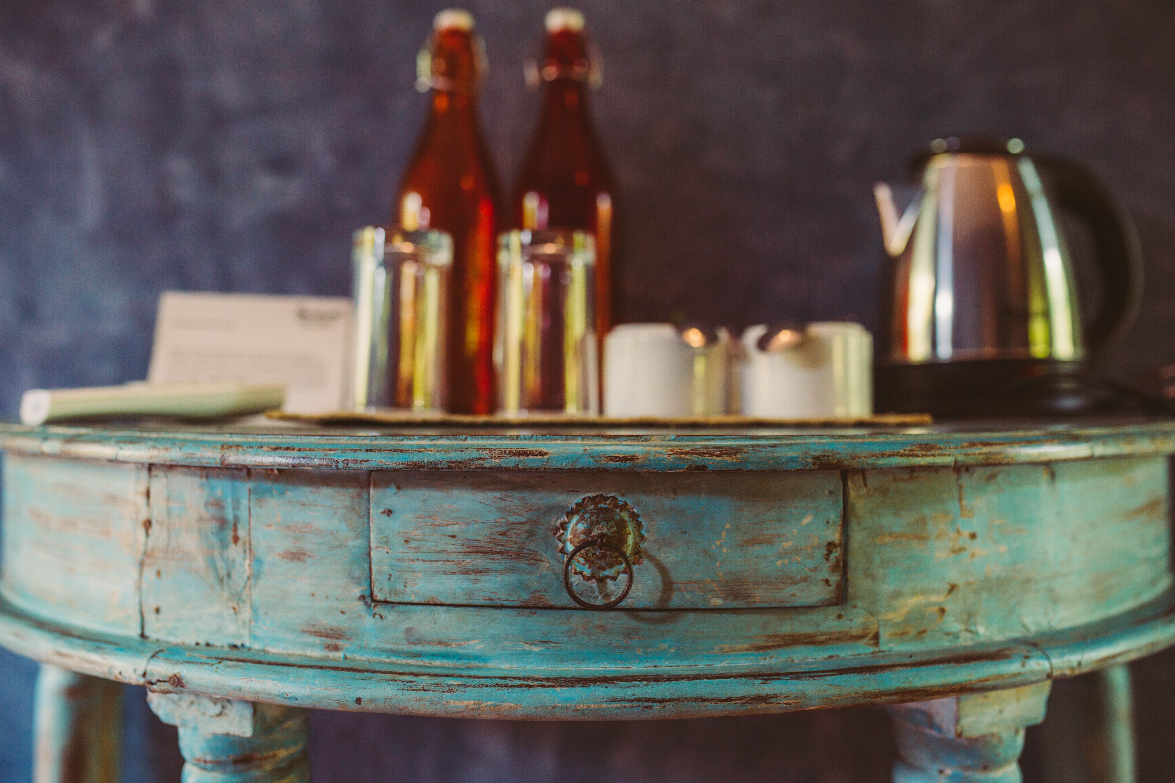 Una mesa rústica color turquesa con diseño vintage, que incluye un cajón y un tirador de metal en forma de anillo.