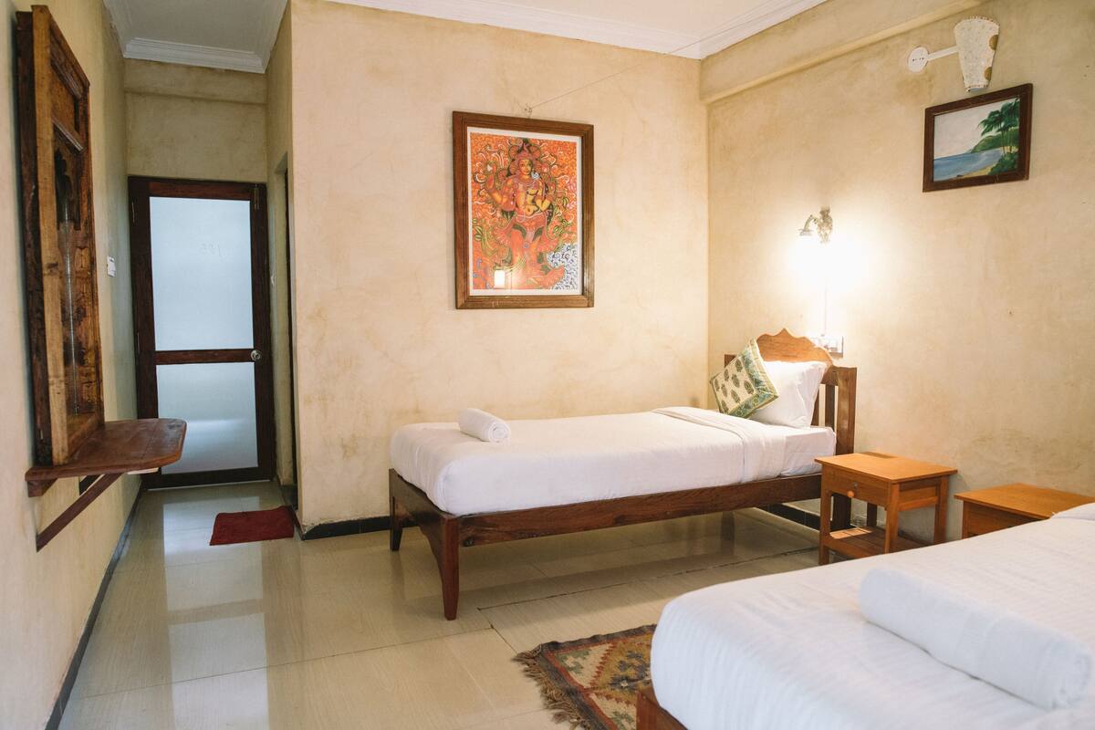A hotel room with a single bed, a wooden nightstand, a wall-mounted lamp, and a painting.
