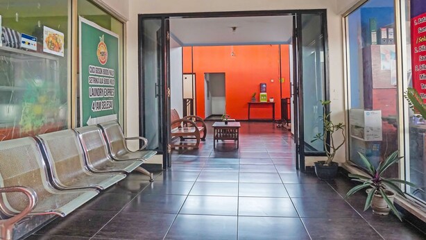 A hotel lobby with a reception desk, seating area, and a bright orange wall. - Hotel O Amazon Homestay Syariah 2 (Tjihadak)