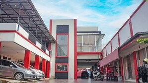 A modern building with a red and white facade, a covered parking area, and a visible motorcycle. - Hotel O Amazon Homestay Syariah 2 (Tjihadak)