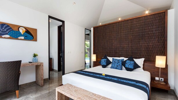 A modern bedroom with a large bed, a wooden headboard, a bench, a desk, and a painting on the wall. - Rent a Luxury Villa in Bali Close to the Beach, Bali Villa 2016 (Seminyak)