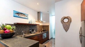 A modern kitchen with a granite countertop, a coffee maker, and a toaster. There is a bowl of fruit on the counter and a fish painting on the wall. - Rent a Luxury Villa in Bali Close to the Beach, Bali Villa 2016 (Seminyak)
