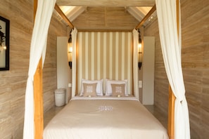 Een slaapkamer met een hemelbed, gestreepte behang en wandlampen.