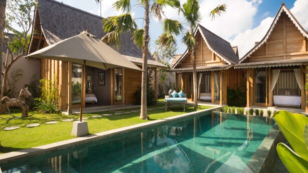 Een zwembadterras met een helder zwembad, houten bungalows en een overdekt zitgedeelte.