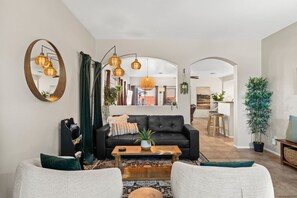 A living room with a black sofa, a wooden coffee table, a mirror, and hanging spherical light fixtures.