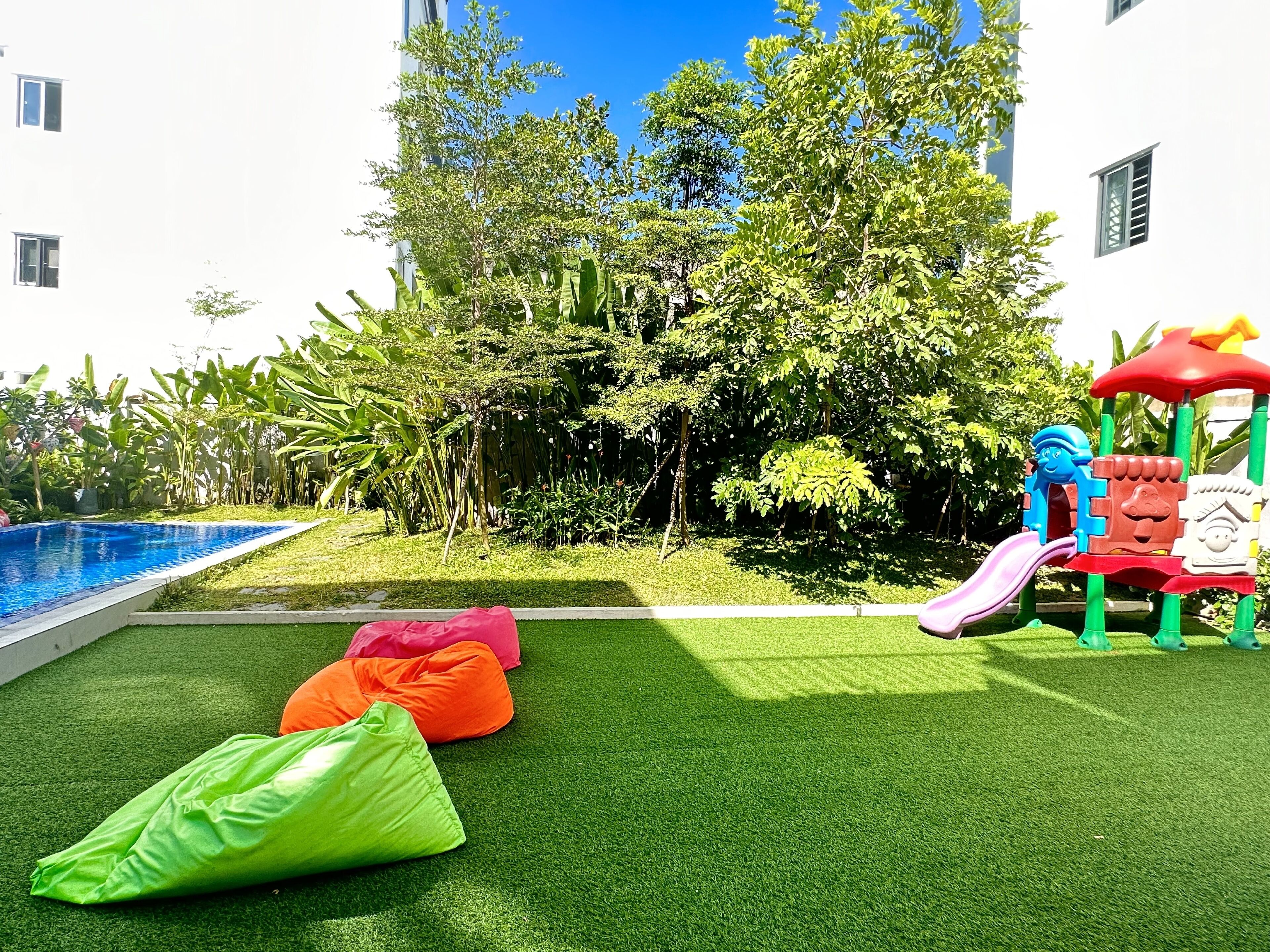 A pool area with artificial grass, colorful bean bags, and a children's play structure.