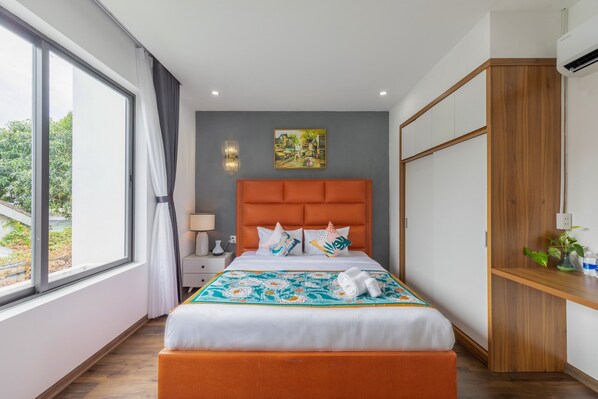 A modern hotel room with a large bed, a wooden wardrobe, a nightstand, and a window with curtains. - MAY CHILL HOUSE VILLA (Da Nang)