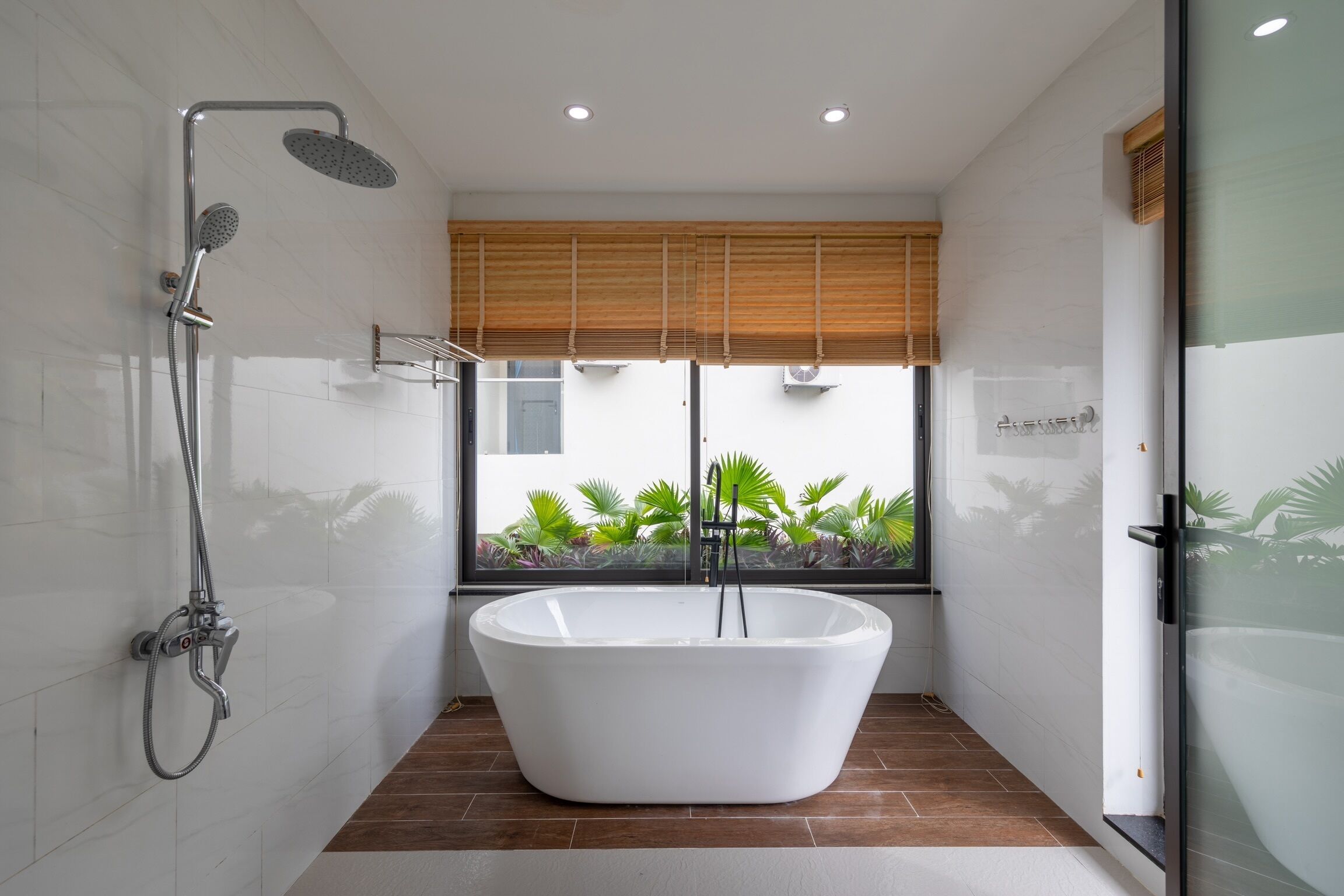 A modern bathroom with a freestanding bathtub, a showerhead, and a window with blinds.