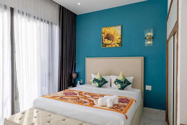 Quarto de hotel com uma cama grande, cabeceira, luminária na parede e um quadro de um girassol.