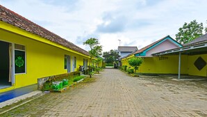 A narrow cobblestone street lined with yellow buildings, each with a tiled roof and a small porch area. - Hotel O Cipto Arum (Cilacap)