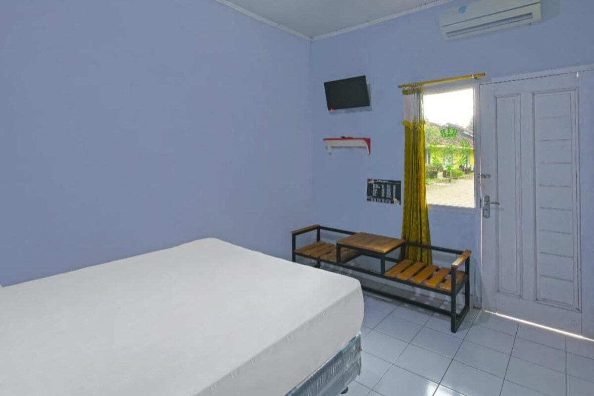Een kamer met een bed, een bureau, een stoel, een televisie en een deur naar buiten.