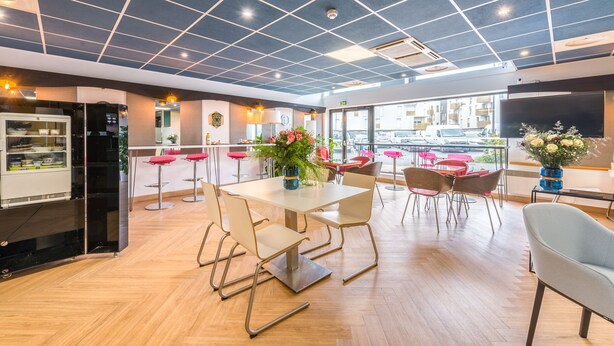 Un comedor moderno con una mesa grande, varias sillas y una zona de cocina con refrigerador y cafetera.