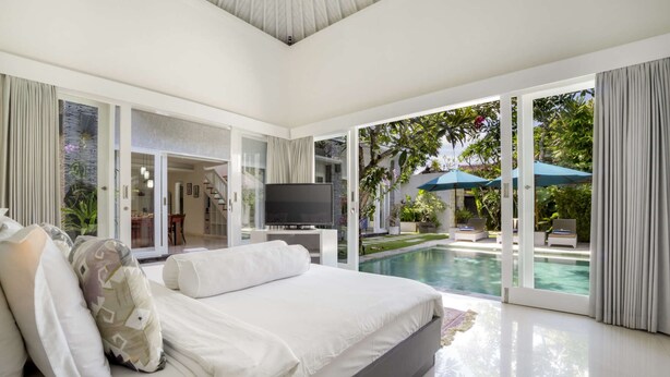 Un dormitorio moderno con una cama grande, un televisor y vistas a una piscina y jardín.