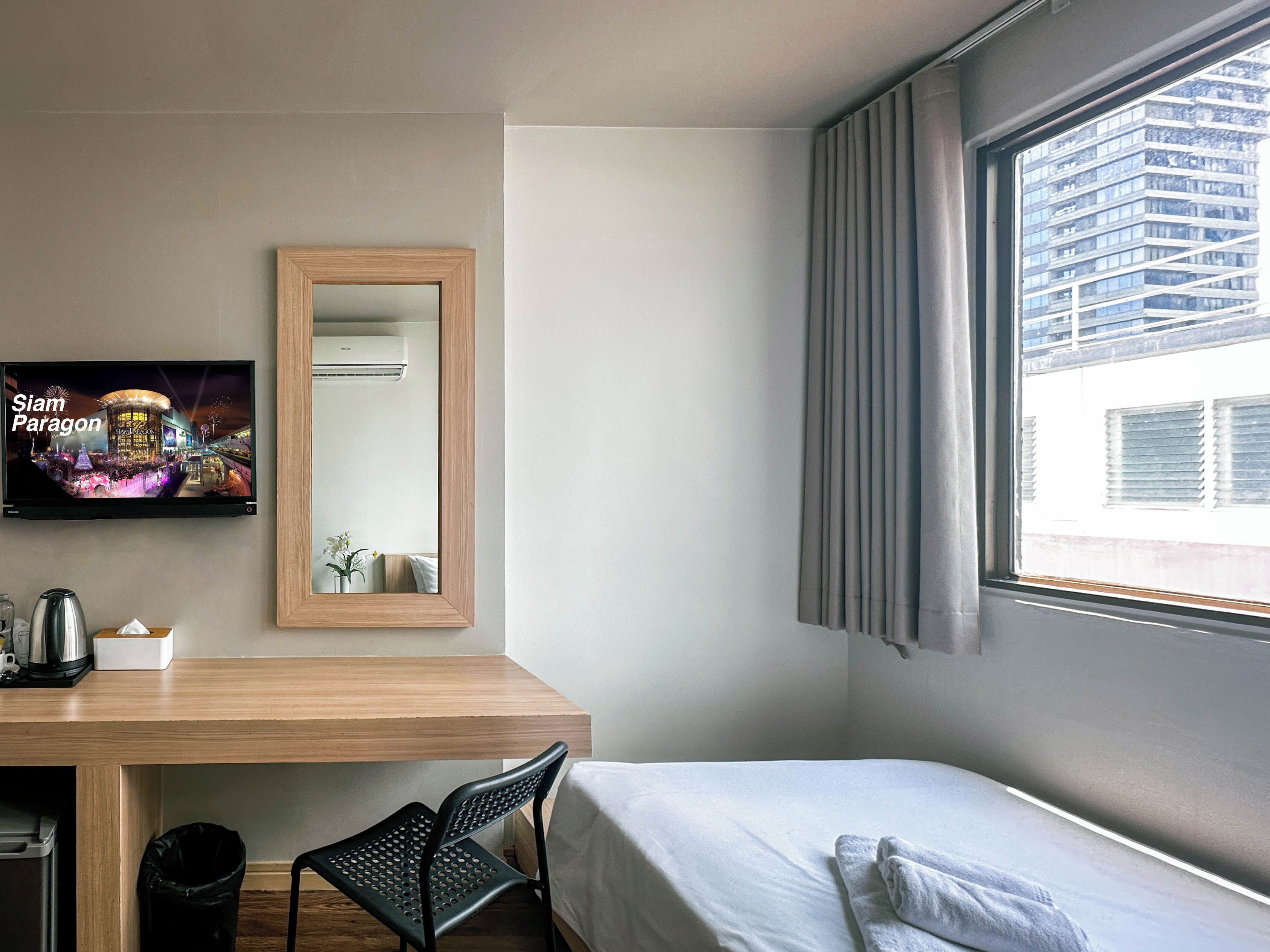 A hotel room with a bed, a desk with a chair, a television mounted on the wall, and a window with curtains.