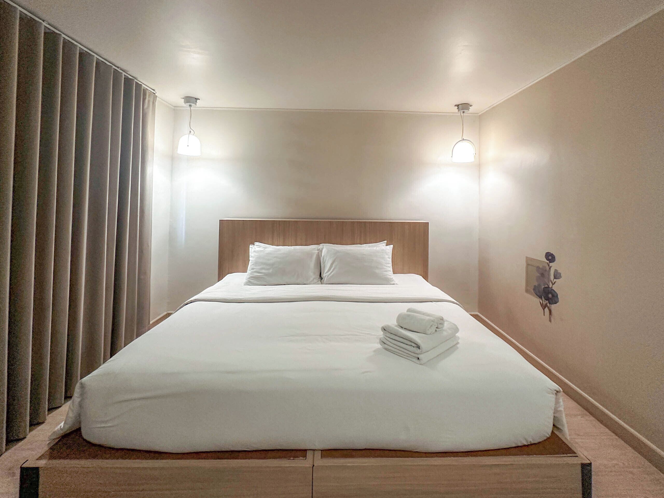 A neatly made bed with white linens, a wooden headboard, and two bedside lamps.