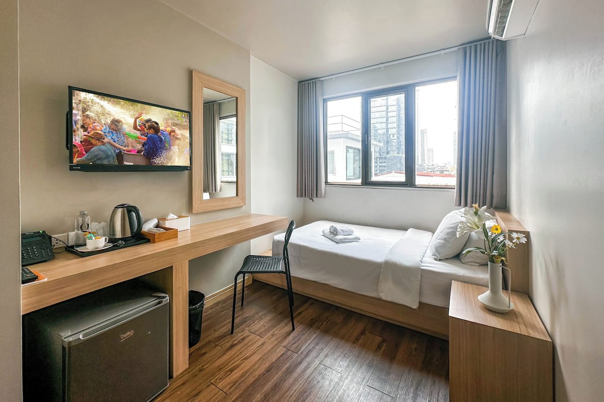 Une chambre d’hôtel compacte comprenant un lit, un bureau, une télévision, une fenêtre avec des rideaux et une petite kitchenette.