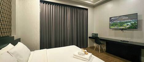 Quarto de hotel com cama, secretária, televisão e vista para um parque.