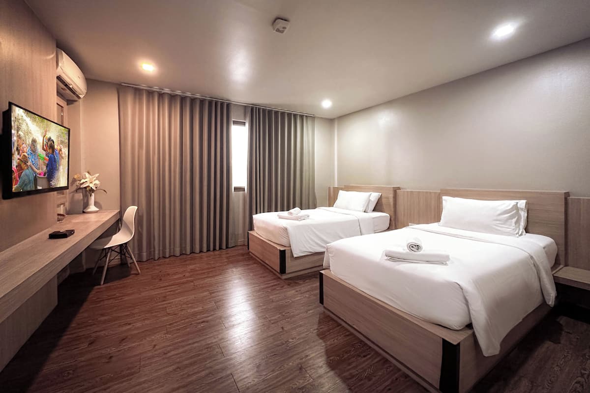 Une chambre d’hôtel avec deux lits, un bureau, une chaise et un téléviseur fixé au mur.
