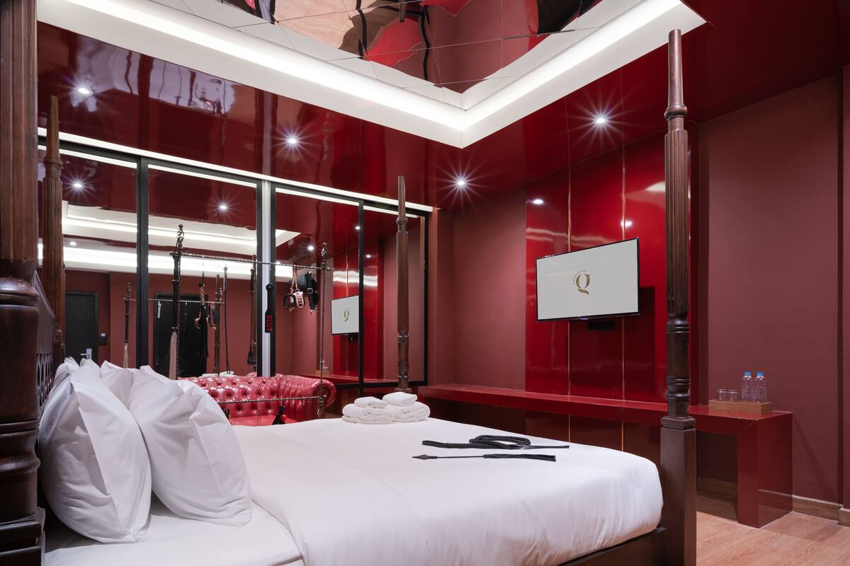 Une chambre d’hôtel moderne avec un grand lit, un canapé en cuir rouge, une coiffeuse avec un miroir et un téléviseur fixé au mur.