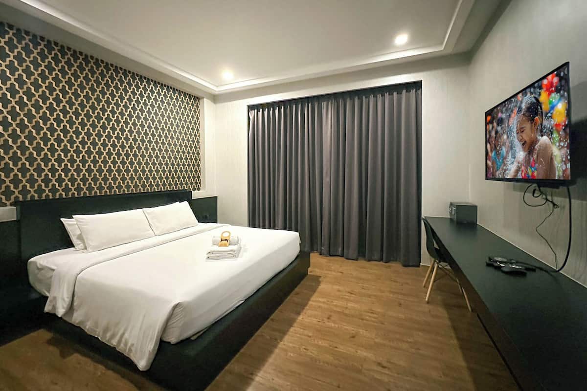 Une chambre d’hôtel avec un lit, un bureau, une télévision et un mur décoré de motifs.