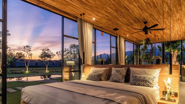 A spacious bedroom with a large bed, wooden ceiling, and large windows offering a view of a landscaped garden and distant mountains. - Sea View Pool House (Buleleng)
