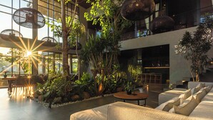 A spacious indoor area with a large seating area, multiple dining tables, and a variety of plants. - Sea View Pool House (Buleleng)