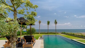 A swimming pool with a view of the ocean, surrounded by palm trees and lounge chairs. - Sea View Pool House (Buleleng)