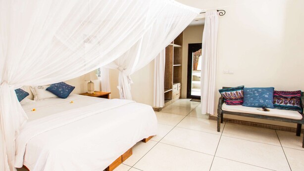 Une chambre à coucher avec un lit à baldaquin, une table de chevet avec une lampe, un banc avec des coussins et une armoire.