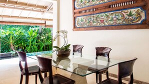 Un coin repas avec une table en verre et quatre chaises, entouré d’une végétation luxuriante et agrémenté d’un panneau décoratif mural.