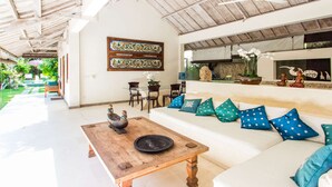 Un vaste espace de vie agrémenté d’un canapé blanc, de coussins aux motifs bleus et blancs, d’une table basse en bois et d’un élément décoratif mural.