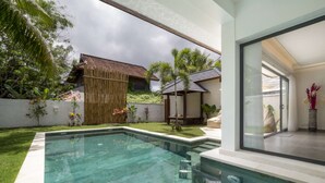 Ein moderner Poolbereich mit klarem Wasser, einer Holzterrasse und Blick auf ein Haus mit einem Ziegeldach und einem Bambuszaun.