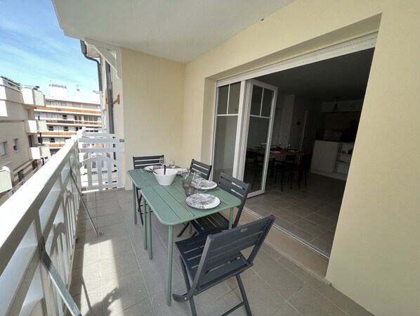 A balcony with a dining table set for two, chairs, and a bowl.