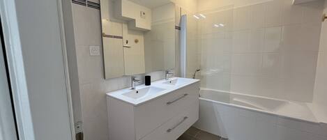 A modern bathroom with a double sink vanity, a large mirror, a bathtub, and a shower area.