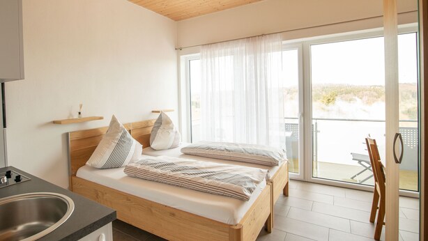 Une chambre avec un lit en bois, un petit coin cuisine et un balcon avec vue.