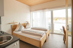 Een slaapkamer met een houten bed, een kitchenette en een balkon met uitzicht.