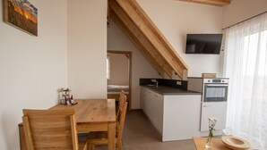 Une cuisine compacte avec une table et des chaises en bois, un petit îlot central doté d’un évier et un téléviseur fixé au mur.