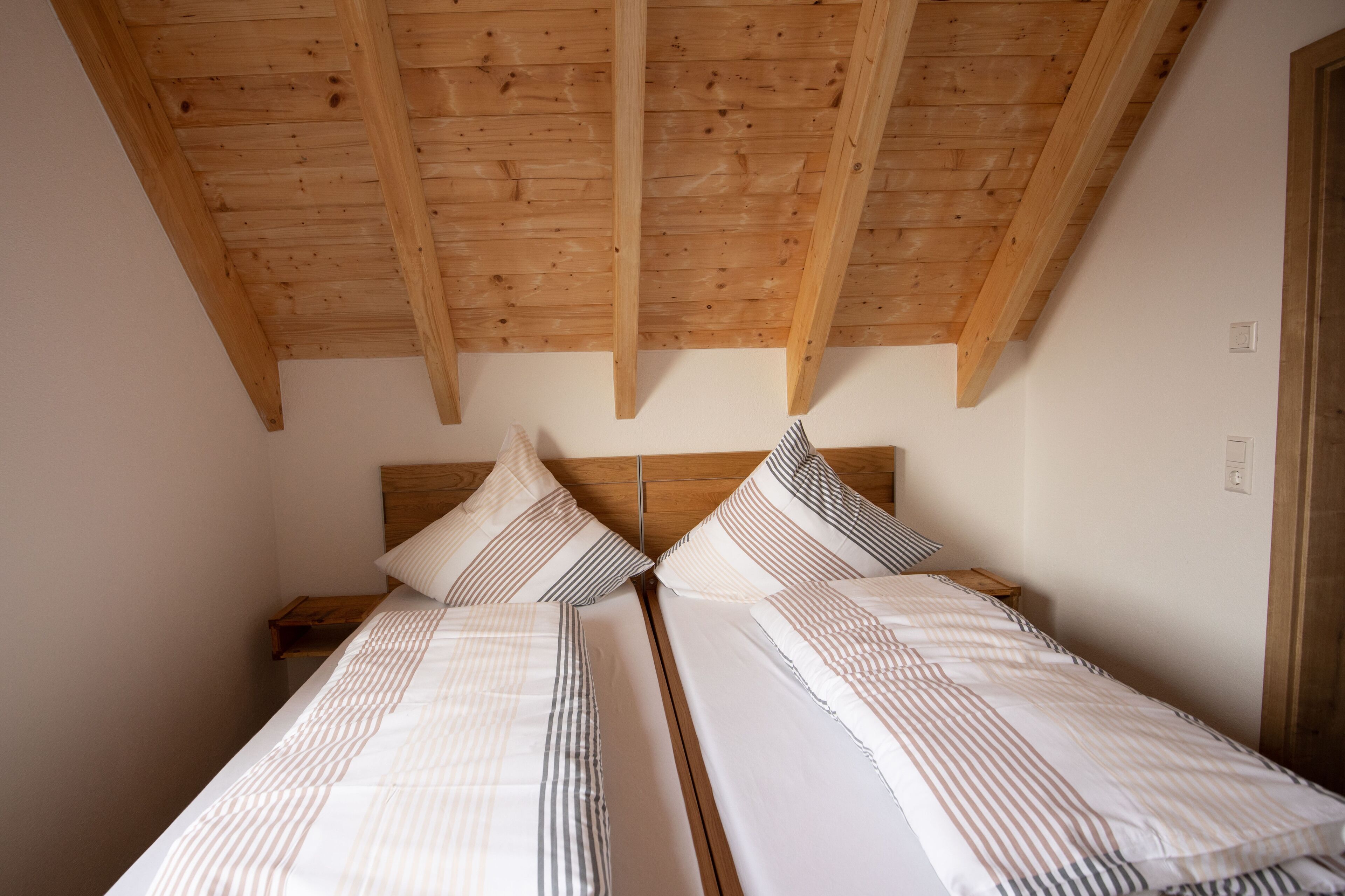 Ein Schlafzimmer mit zwei Betten, Holzbalken an der Decke und einem Nachttisch.