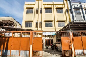 A multi-story building with a central entrance, a sign indicating 'Kota Residence', and a gated parking area with motorcycles.