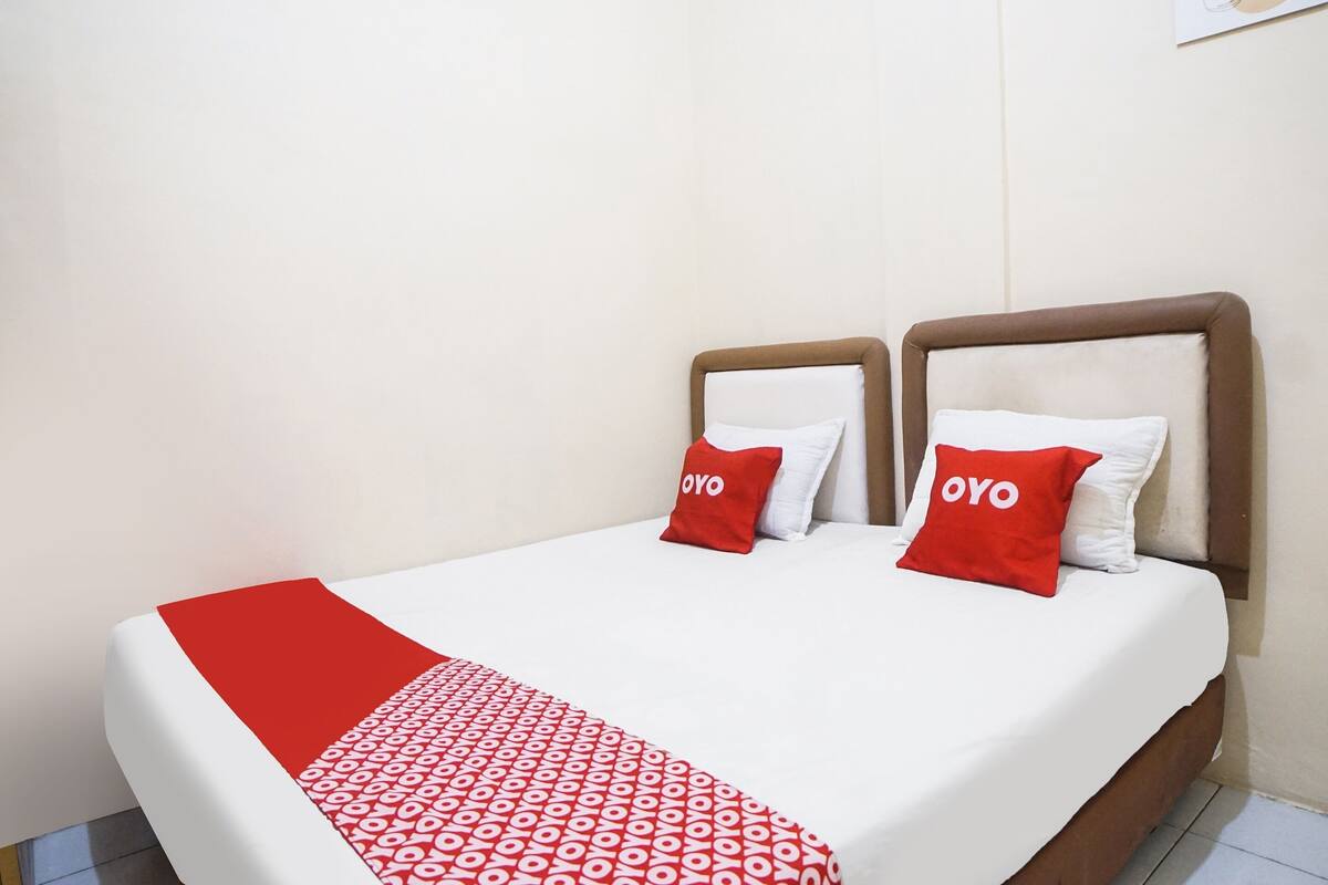 Een tweepersoonsbed met een rood-witte spreideken en twee rode kussens met de tekst 'OYO'.