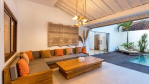 A modern living room with a sectional sofa, a wooden coffee table, and a large decorative wall hanging. - Wonderful 4BR Villa With Pool, Bali Villa 2212 (Seminyak)