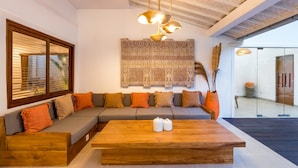 A modern living room with a wooden coffee table, a grey sofa with orange cushions, and a patterned tapestry on the wall. - Wonderful 4BR Villa With Pool, Bali Villa 2212 (Seminyak)