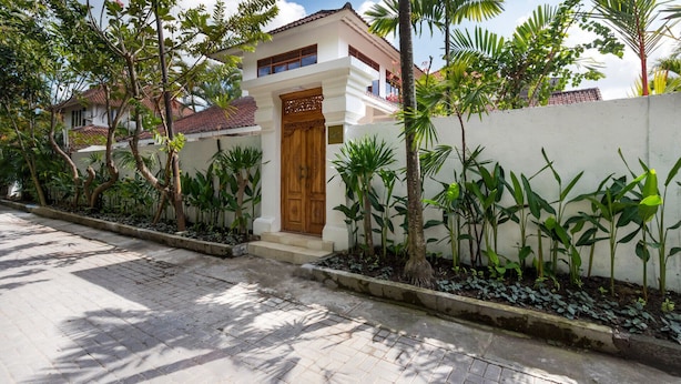A two-story house with a wooden door, surrounded by a white wall and various tropical plants. - Wonderful 4BR Villa With Pool, Bali Villa 2212 (Seminyak)