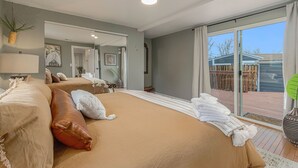 Une chambre avec un grand lit, un miroir et une porte-fenêtre coulissante donnant sur une terrasse extérieure.