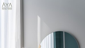 Una habitación moderna con un espejo redondo, un cojín estampado de pata de gallo y un marco de foto sobre una consola blanca.