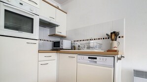 A compact kitchen with white cabinets, a microwave, a dishwasher, and a wooden countertop. - Bright Apartment Near Beach with Parking, Balcony & Modern Amenities – Stella (Cucq-Stella Plage)