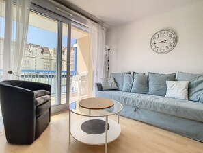 Een moderne woonkamer met een bank, een ronde salontafel en een groot raam met uitzicht op gebouwen.
