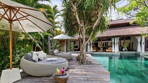 Un espace aménagé au bord de la piscine, avec une terrasse en bois, des sièges d’extérieur et une vue dégagée sur la piscine.