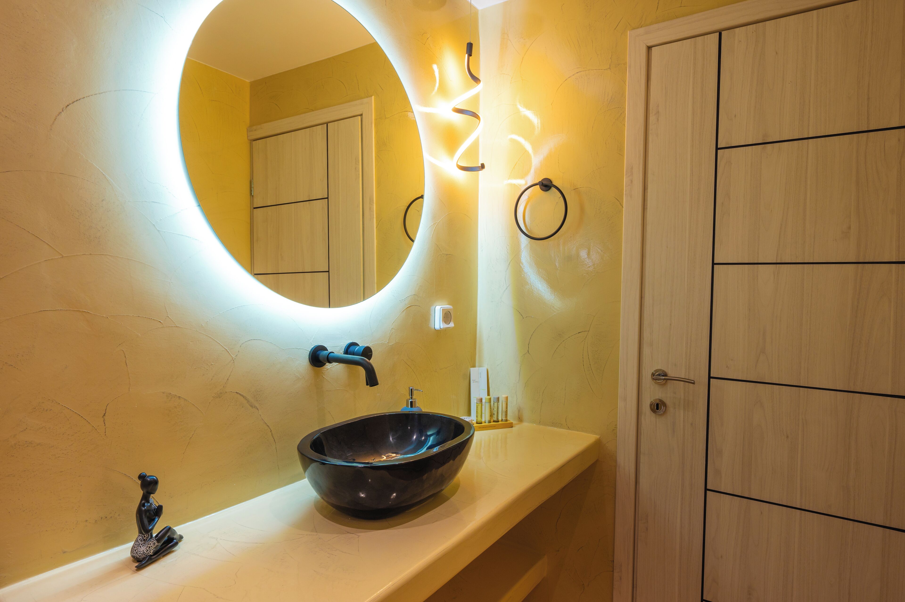 A bathroom with a round mirror, a black vessel sink, and a wooden door.