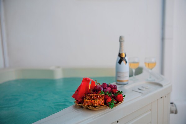 A poolside setting with a bottle of champagne, glasses, and a basket of fruit. - Aina Suites (Santorini)